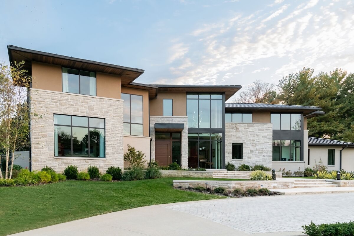 2 Homes by Beth Haley Design: A Study in Style & Contrast - 1 Modern two-story house by Beth Haley Design, featuring large windows, a stone and wood exterior, and a landscaped front yard.
