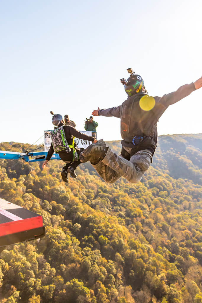 The Best Festivals in the South - 20 Two people wearing gear jump off a platform with a forested valley below, capturing the scene with cameras on their helmets, as part of an exhilarating festival experience in the South.