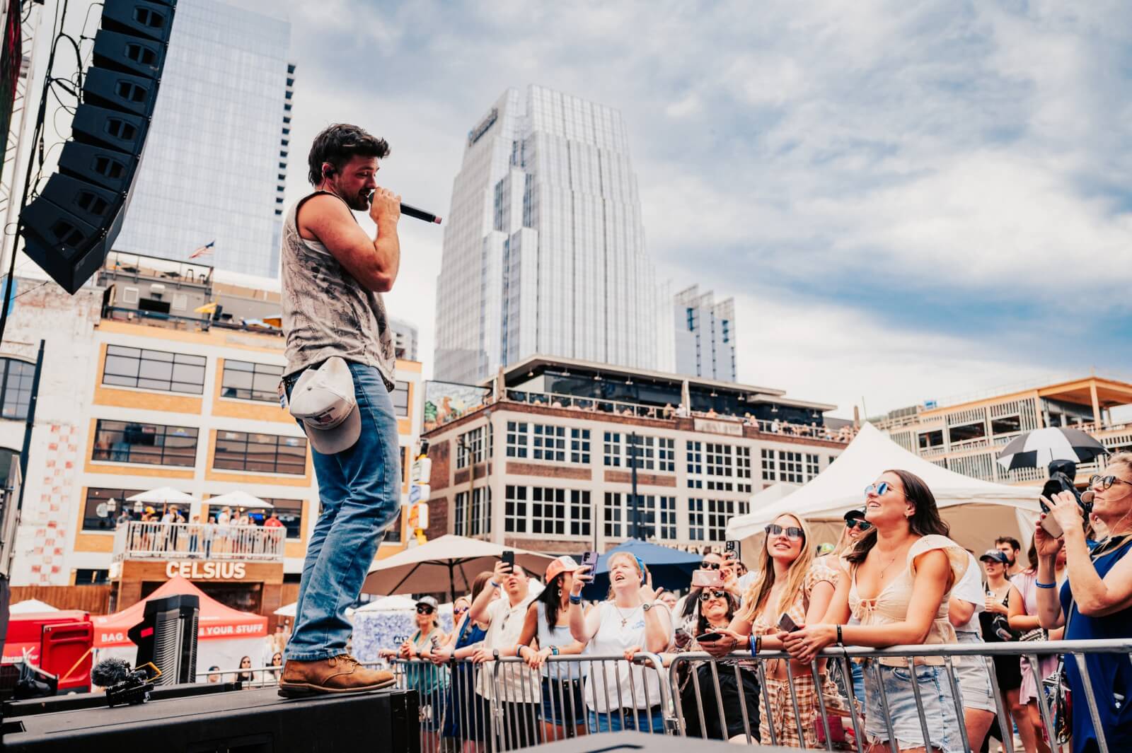 The Best Festivals in the South - 10 A singer captivates the audience on an outdoor stage, set against the backdrop of urban buildings and a cloudy sky. The vibrant performance evokes the lively spirit typical of southern festivals.