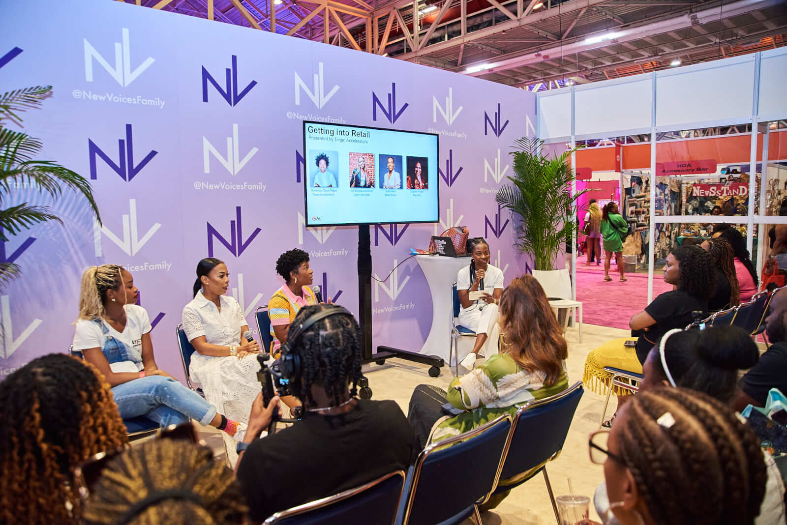 The Best Festivals in the South - 14 A panel of women speaks to an audience at an event in the South, featuring a screen with speaker photos. The backdrop proudly displays "New Voices Family" branding, capturing the essence of community festivals and celebrations.