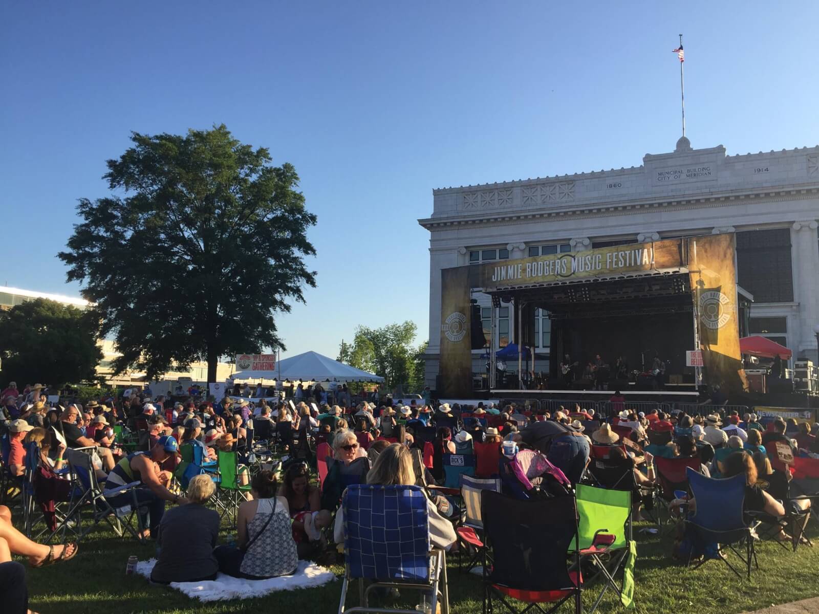 The Best Festivals in the South - 6 At one of the best festivals in the South, a large crowd is seated on grass, soaking up the sun as musicians perform under the "Jimmie Rodgers Music Festival" banner.