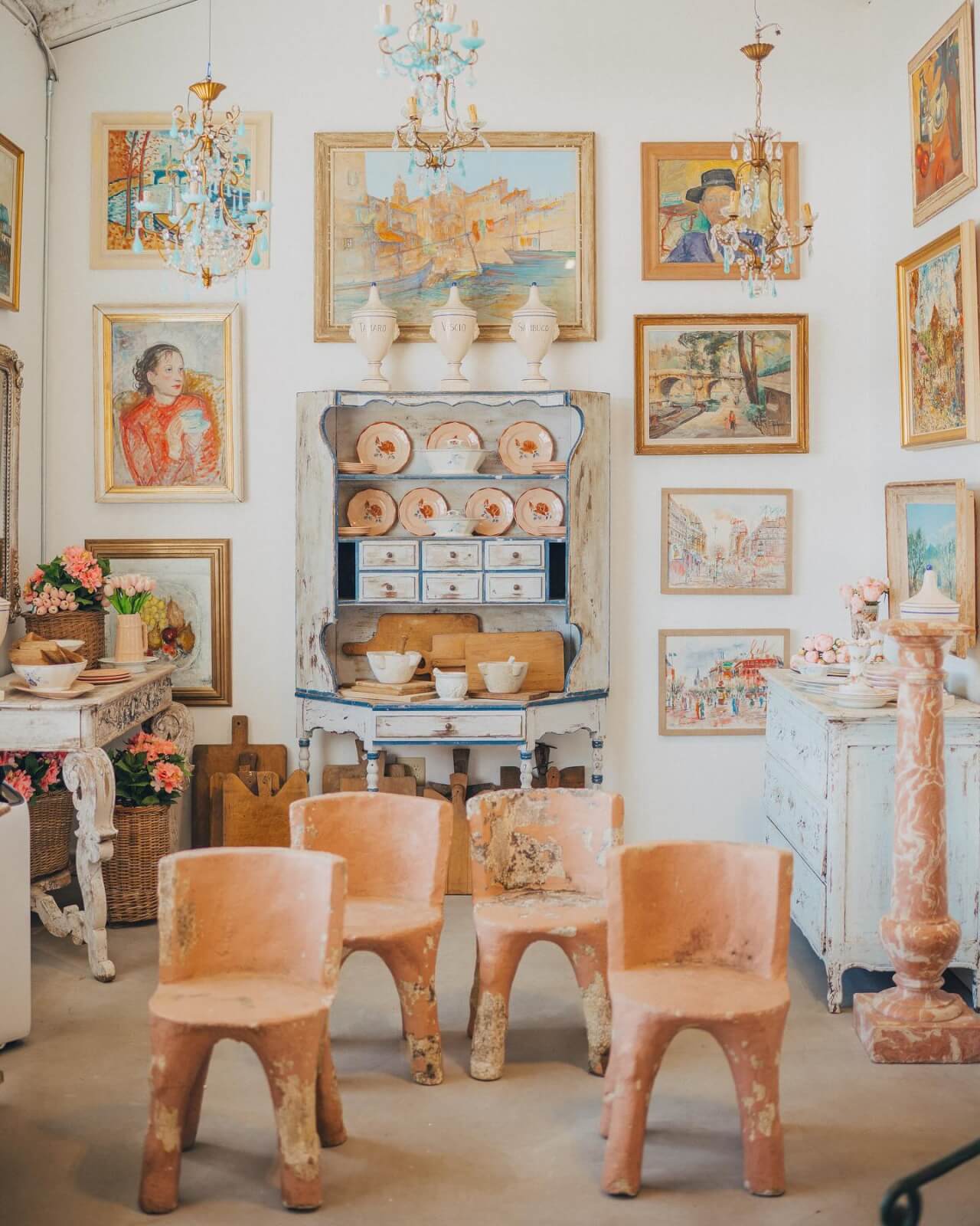 The Best Festivals in the South - 19 A vintage-style room with terracotta chairs, framed paintings on the wall, and chandeliers evokes a Southern charm. The white hutch displays pottery and various decorative items.