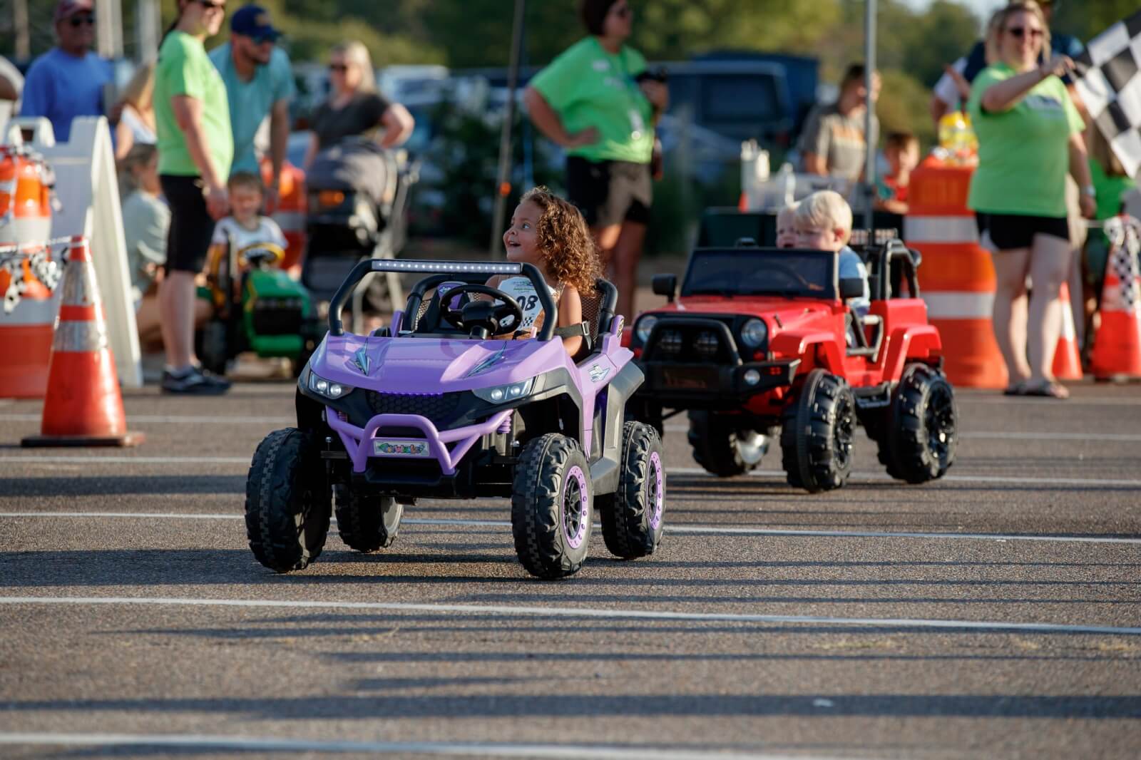 The Best Festivals in the South - 16 Children driving toy cars on an outdoor track at a lively festival in the South, with onlookers and traffic cones scattered in the background.