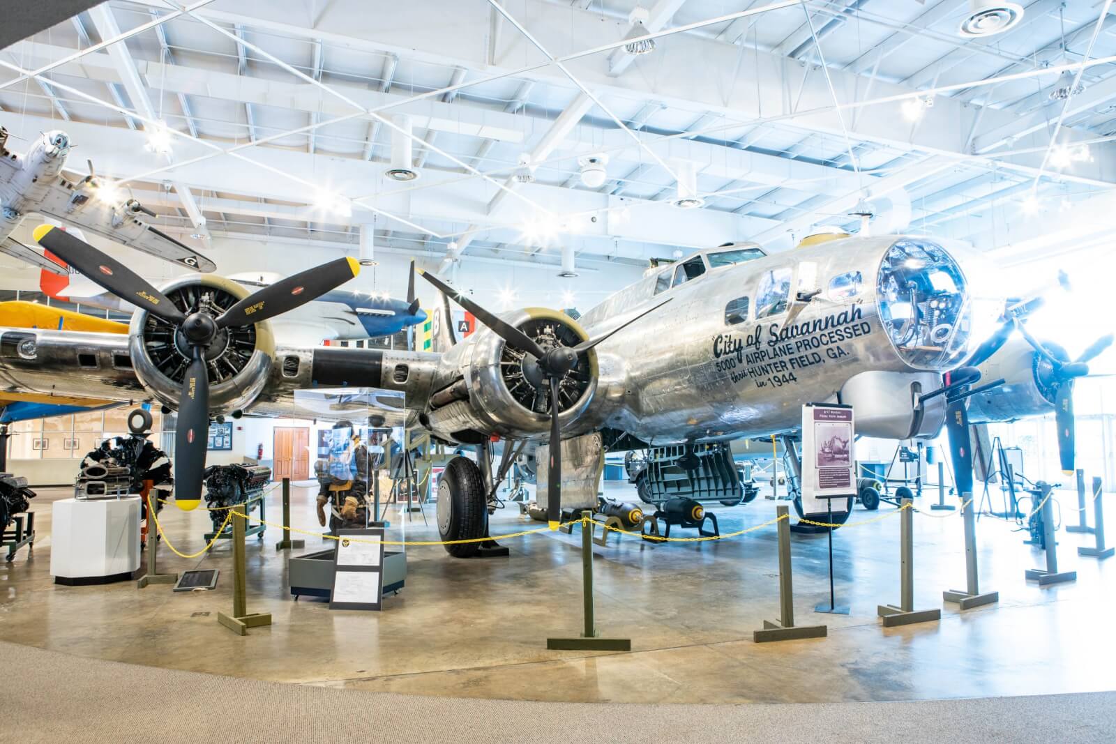 A shiny, restored World War II B-17 bomber is displayed indoors at a museum in the South, surrounded by informational signs and protective barriers.