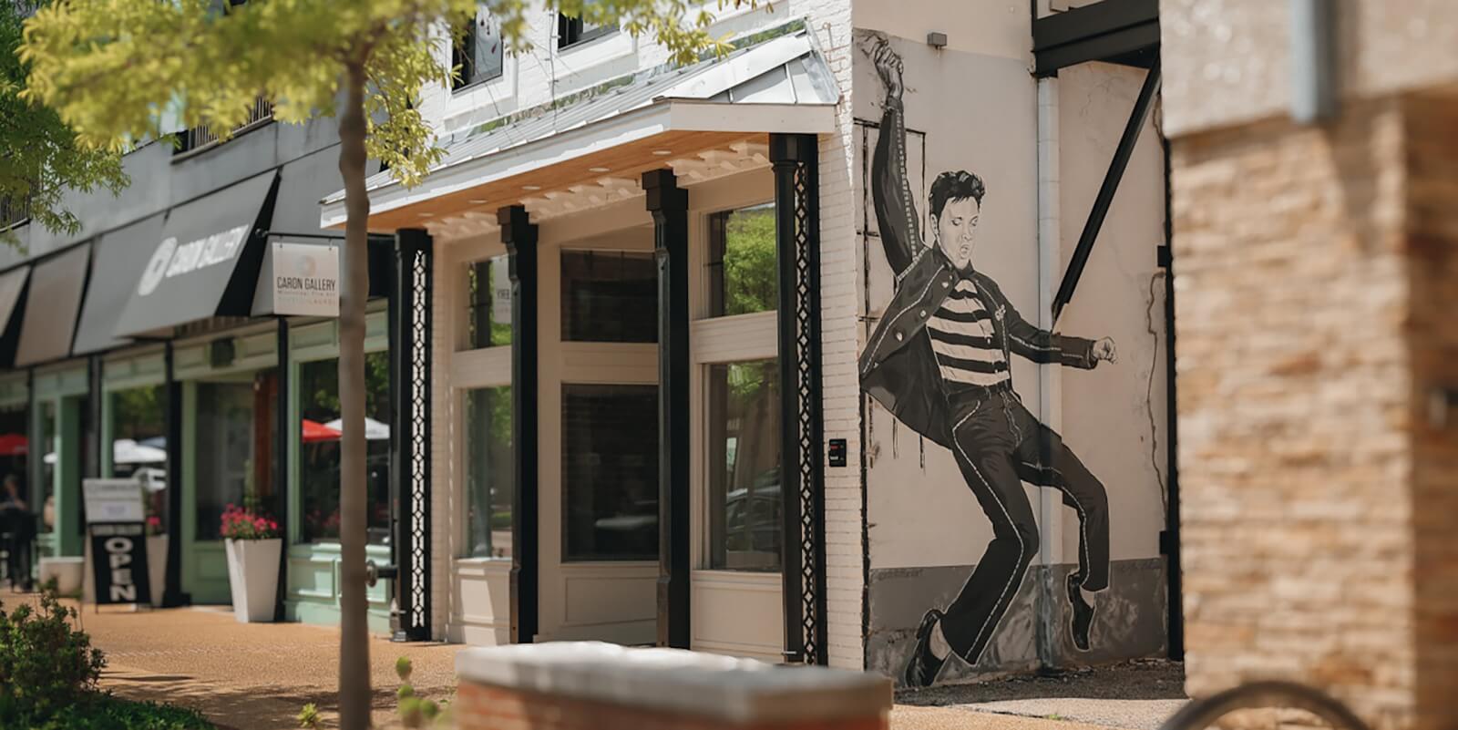 A black-and-white mural of a dancing man in a striped shirt and jacket decorates the exterior wall of a downtown building, just steps away from some of the Best Trails along the popular Hiking South route.