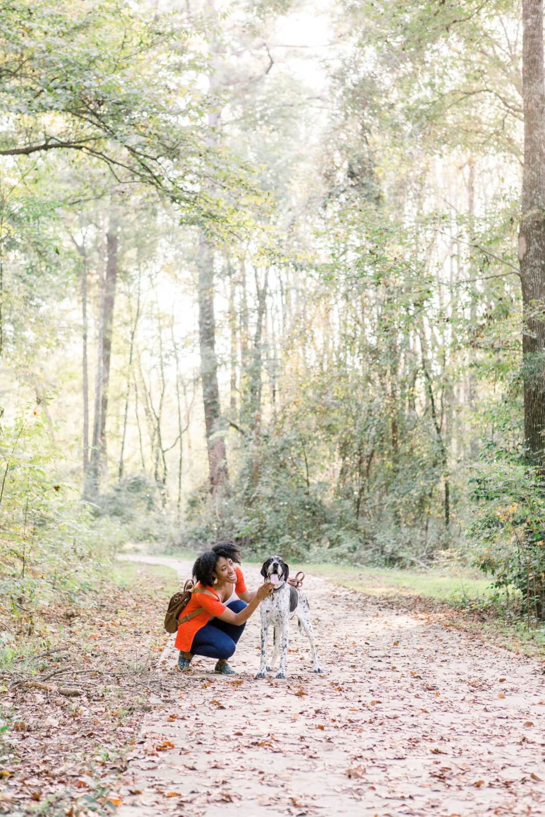Georgia's 6 Best Girlfriends' Weekend Getaways - 16 A person in a red shirt kneels and pets a dog on a forest trail in Georgia, lined with trees and fallen leaves—an idyllic moment perfect for those seeking the best getaways.