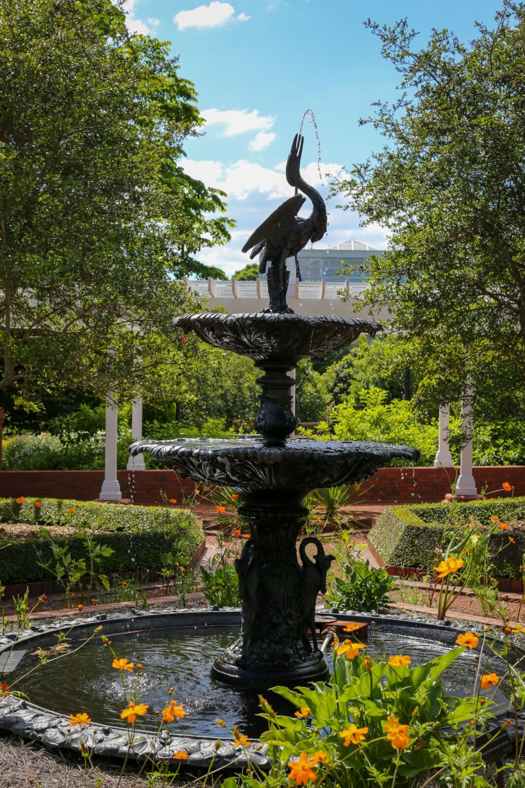 Georgia's 6 Best Girlfriends' Weekend Getaways - 5 A black bird-shaped fountain stands in a garden with yellow flowers, trimmed hedges, and trees under a partly cloudy sky.