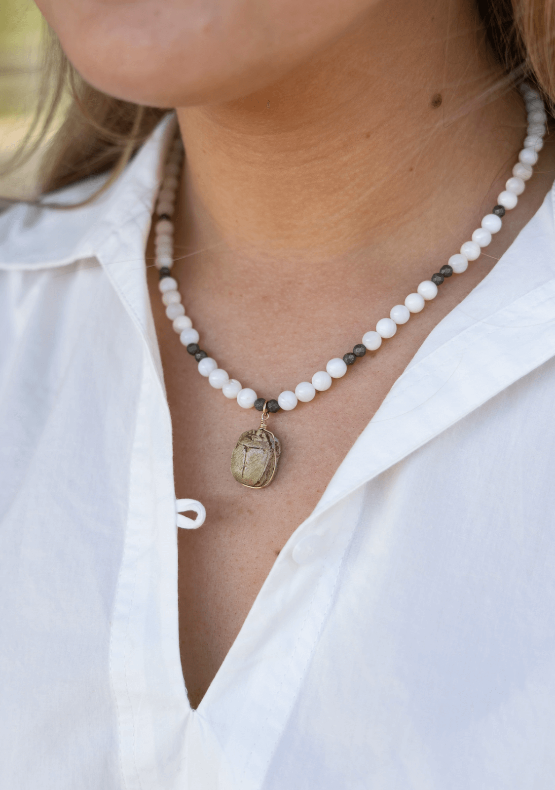 In Birmingham this May, a person wears a white collared shirt and a beaded necklace with a scarab beetle pendant.