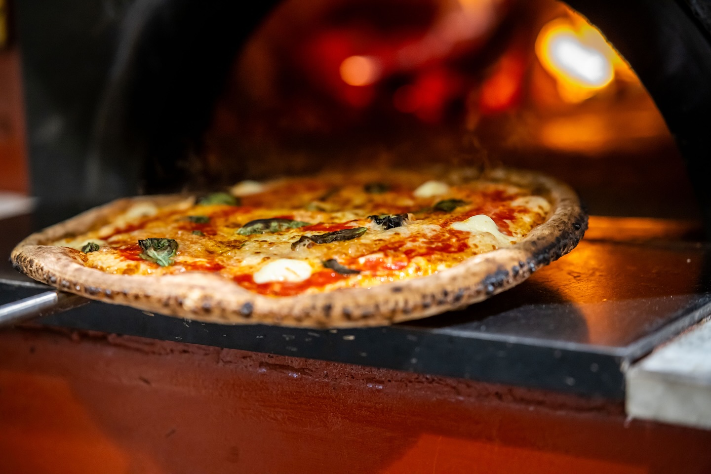 A freshly baked pizza with melted cheese and basil is being taken out of a wood-fired oven at one of Birmingham’s new restaurants.
