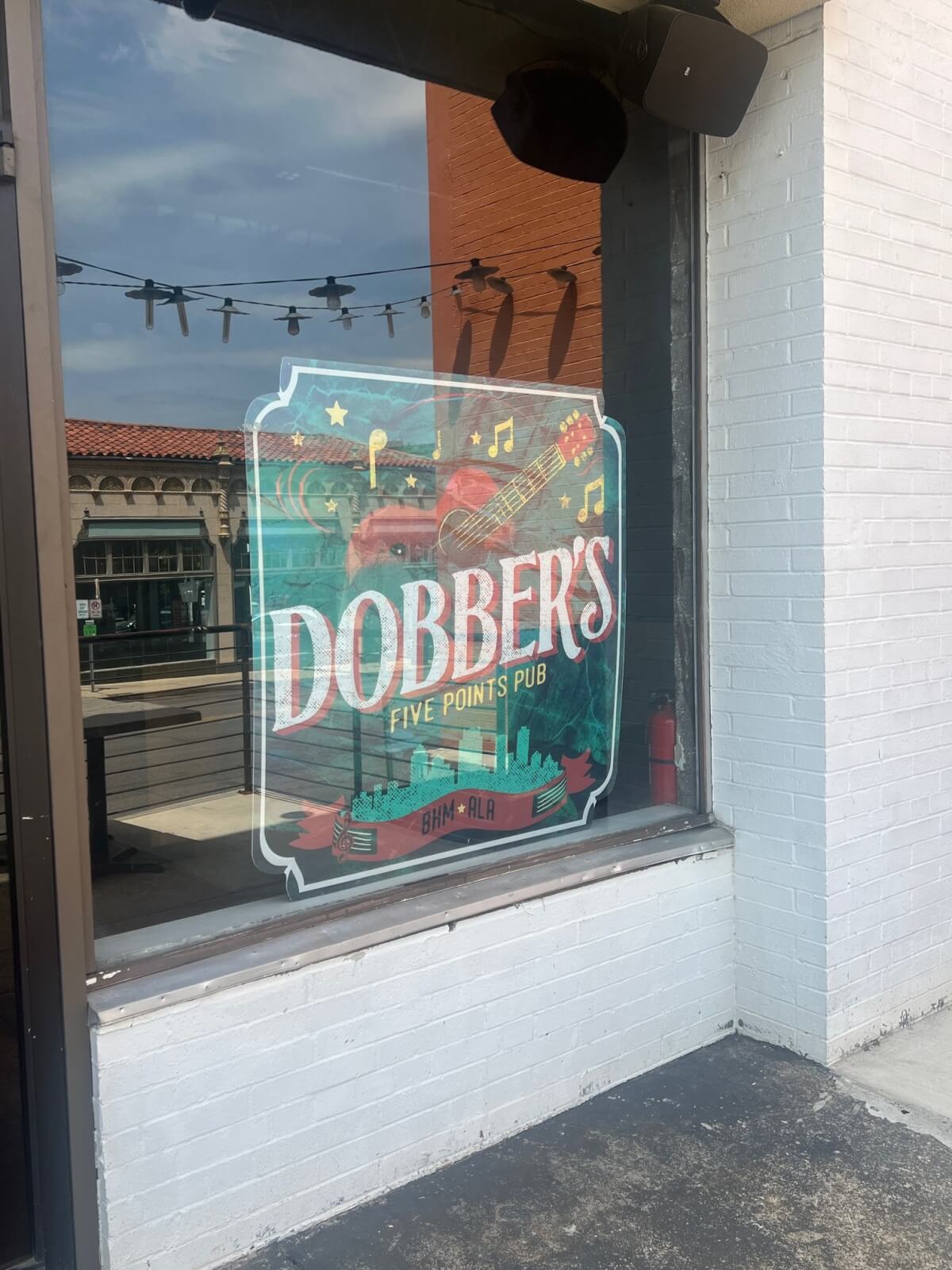 A colorful sign on a window reads "Dobber's Five Points Pub BHM-ALA," with illustrations of a guitar, beer mug, and city skyline—a vibrant nod to Birmingham’s lively restaurants scene.