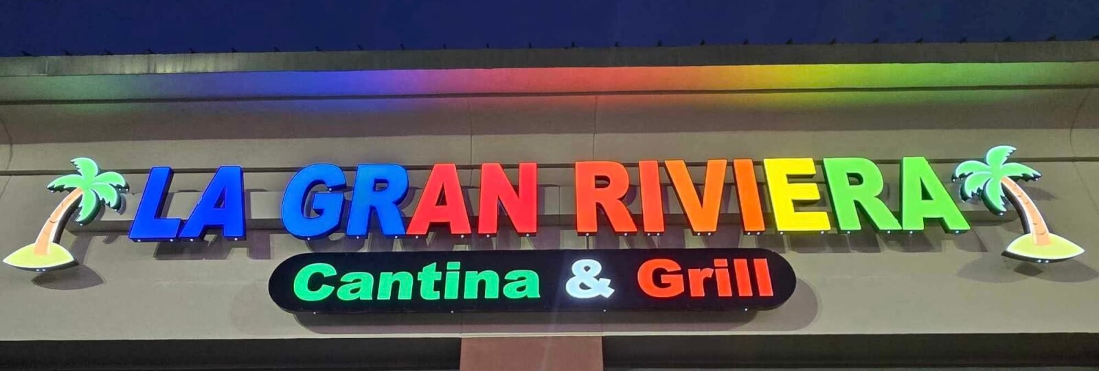 The sign for "La Gran Riviera Cantina & Grill," a vibrant new dining spot in Birmingham, is displayed in colorful, illuminated letters with palm tree graphics on each side.