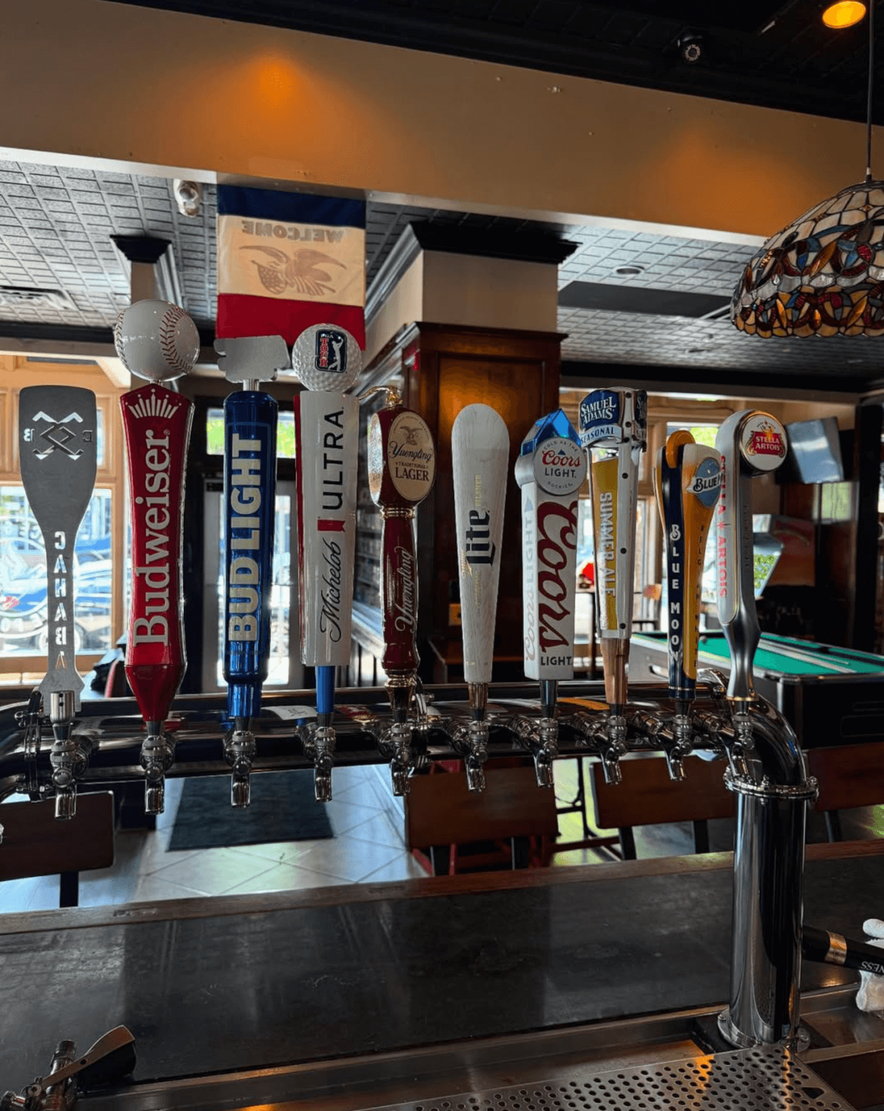 A row of nine draft beer taps at a bar, each labeled with a different brand like Budweiser and Yuengling—a perfect spot for sampling brews at one of the Birmingham restaurants you’ll want to add to your list of restaurants to try.