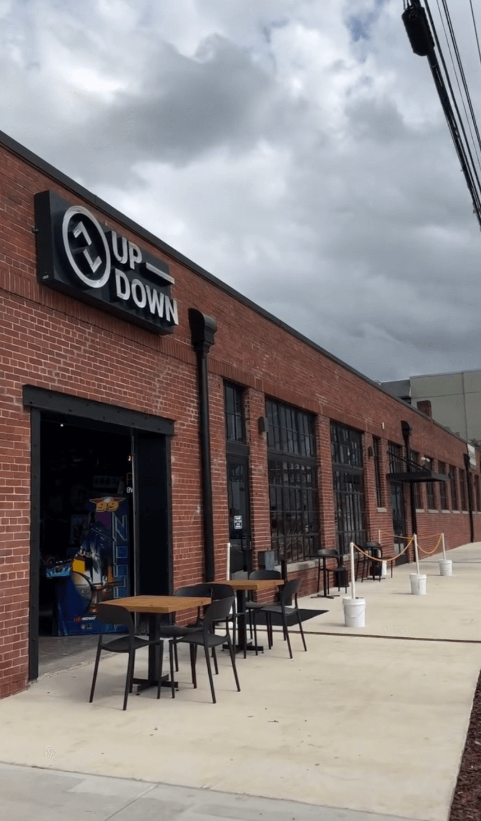 A brick building in Birmingham with a sign reading "UP DOWN" above an open door reveals arcade machines inside; outdoor tables and chairs are set on the adjacent sidewalk, making it one of the city's lively new restaurants.