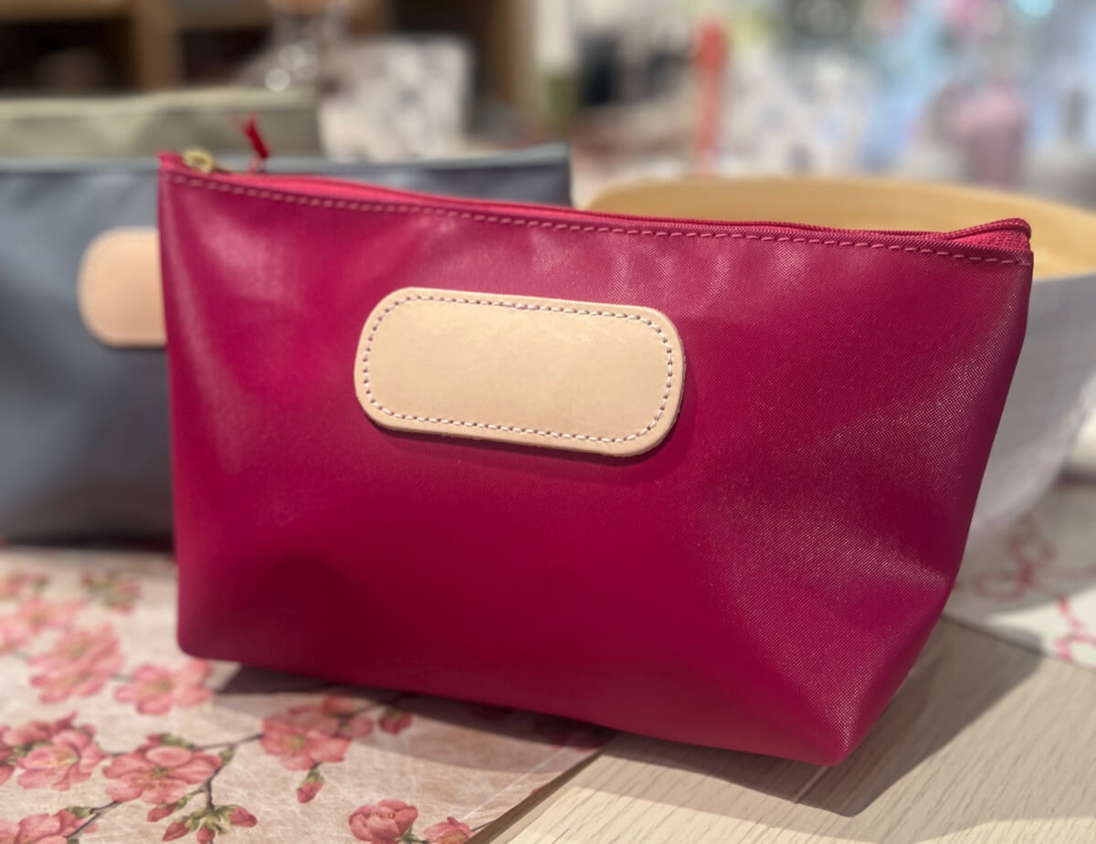 A pink zippered pouch with a beige rectangular patch sits on a table next to a gray pouch and floral-patterned items—perfect for your May FINDS in Birmingham.