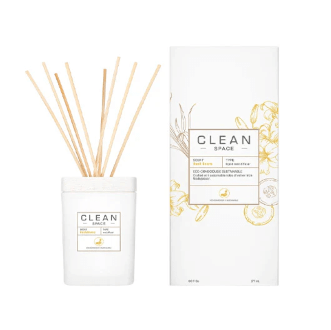 A white Clean Space reed diffuser with sticks sits beside its matching white and gold box featuring floral illustrations