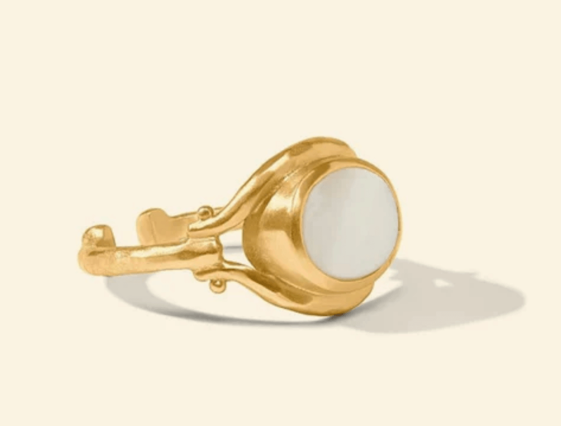A gold ring with an open band design, featuring a round white stone set in the center. Displayed on a neutral background for timeless elegance.