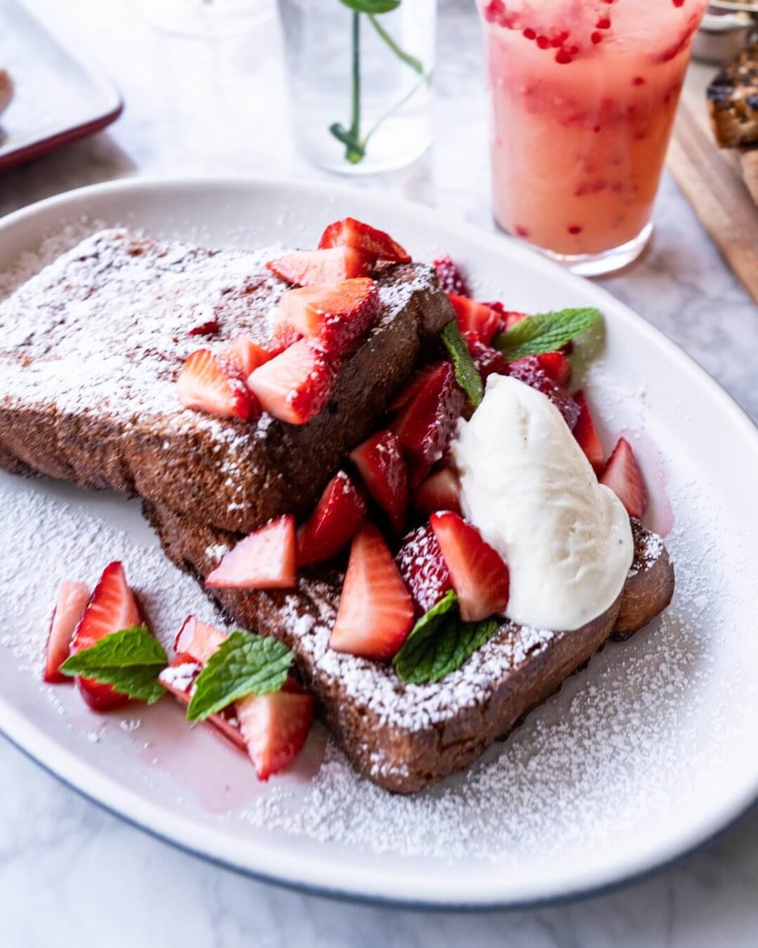 Two slices of French toast topped with powdered sugar, fresh strawberries, mint leaves, and a dollop of whipped cream—perfect for your Mother's Day brunch in Birmingham, AL.
