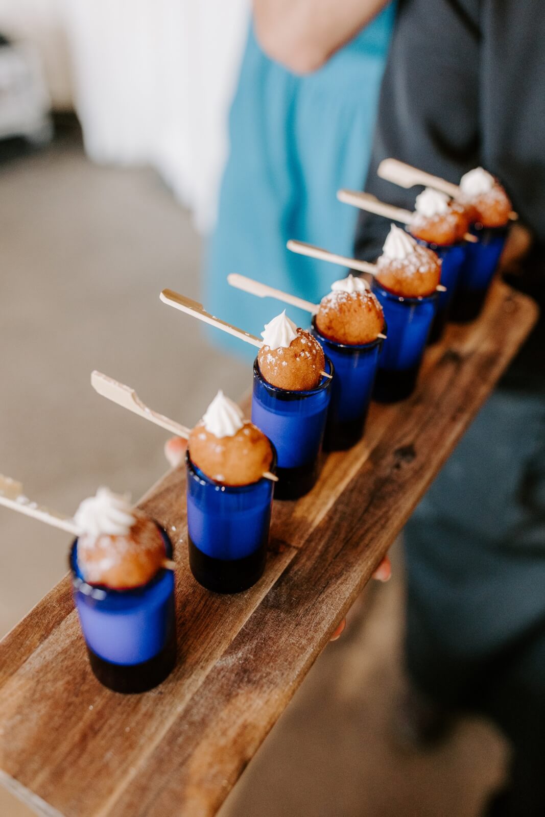 A row of blue shot glasses with desserts topped with whipped cream and skewers, arranged on a wooden serving board—perfect for a Homewood brunch wedding or second line sendoff celebration.