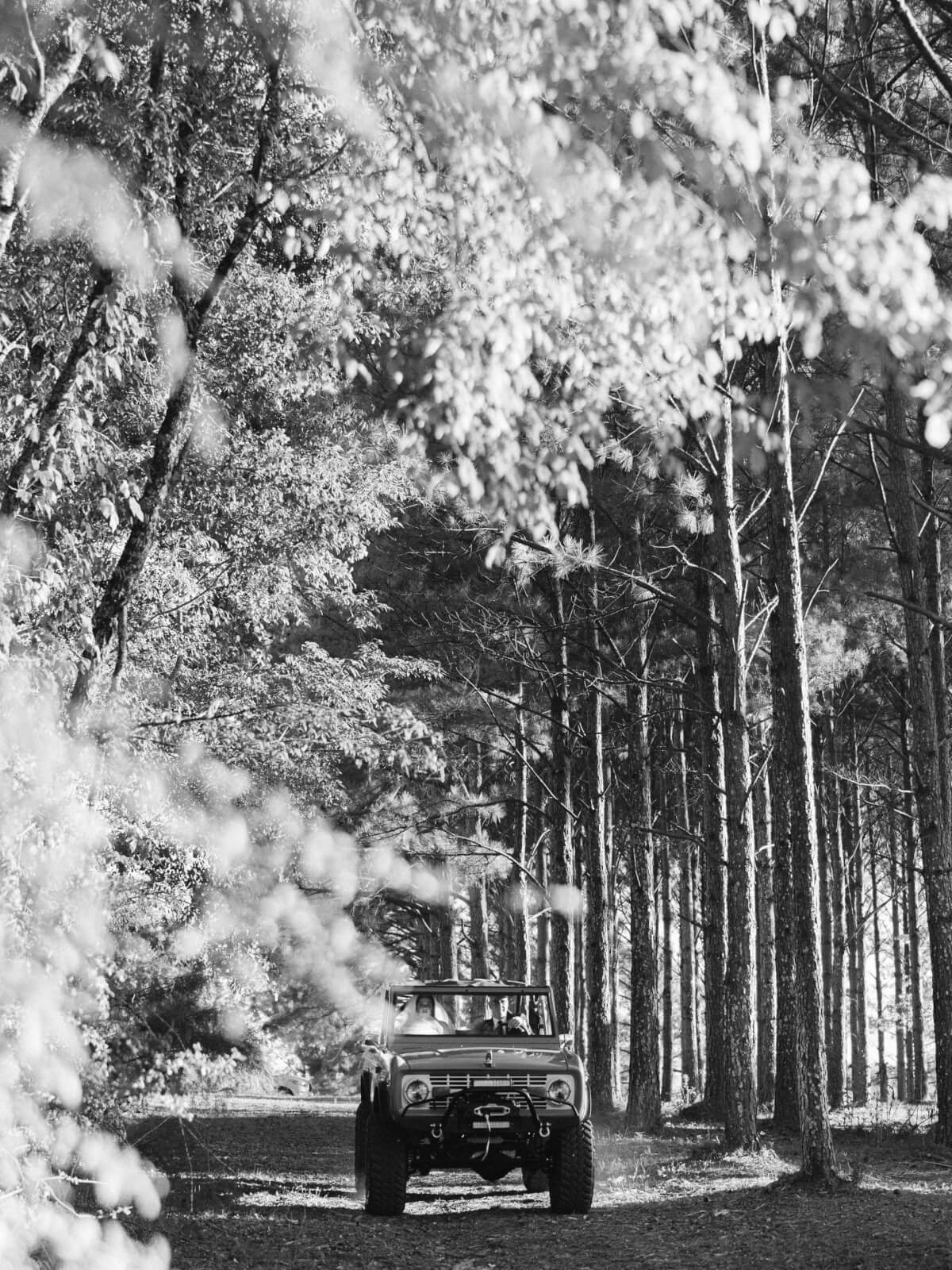 A black and white image captures the father of the bride driving the bride to the ceremony site in a Ford Bronco.