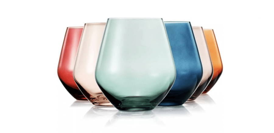 12 Colored Glass Accessories We Love: Cake Stands, Candlesticks & More - 12 A set of six colored glass items, perfect for your spring wish list, showcases vibrant stemless wine glasses in pink, light brown, green, blue, dark blue, and amber. These stunning pieces are elegantly arranged in a semi-circle on a pristine white background.