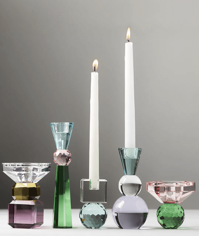 12 Colored Glass Accessories We Love: Cake Stands, Candlesticks & More - 4 Five vibrant geometric glass candleholders cradle two glowing white taper candles against a neutral backdrop.