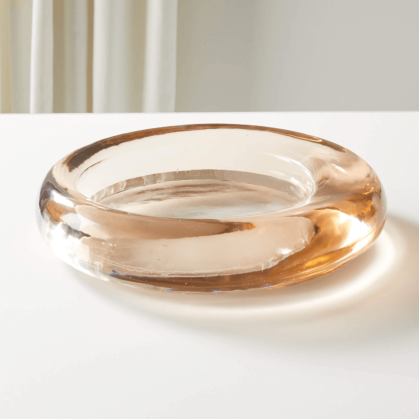 12 Colored Glass Accessories We Love: Cake Stands, Candlesticks & More - 3 This circular amber-tinted ashtray, a standout among colored glass items, rests elegantly on a white surface with a partially visible curtain in the background.