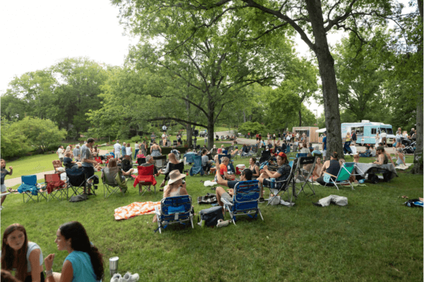 People relax on lawn chairs and blankets in a park, gathering in groups under trees with a food truck nearby—enjoying the vibrant atmosphere of Cheekwood events during Community Week.