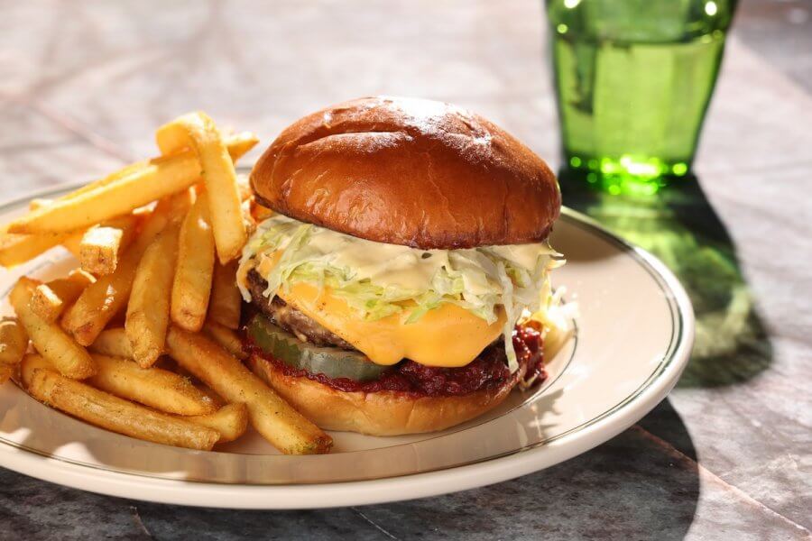 A cheeseburger with lettuce and sauce on a bun is served with French fries on a plate, next to a green glass of water—classic comfort from one of the best new Louisville restaurants.