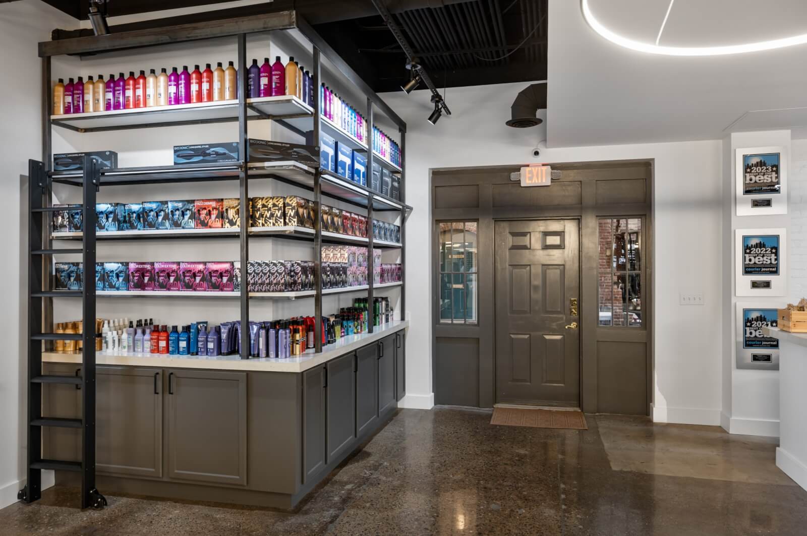 The interior of this Louisville retail store is vibrant, with shelves brimming with colorful hair and beauty products. A ladder leans against the displays, while awards proudly adorn the wall by the gray entrance door—a perfect showcase of TRIM NuLu's excellence.