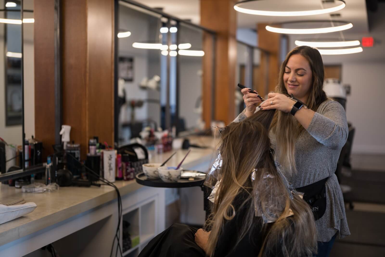 In a chic Louisville salon, a stylist expertly applies hair dye to a seated client's hair.