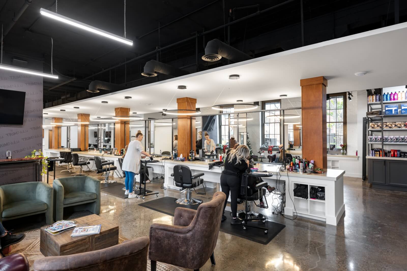 TRIM NuLu, a chic hair salon in Louisville, boasts modern stylists who skillfully attend to clients. The space features sleek chairs, large mirrors, and a diverse array of hair products on display for all your styling needs.