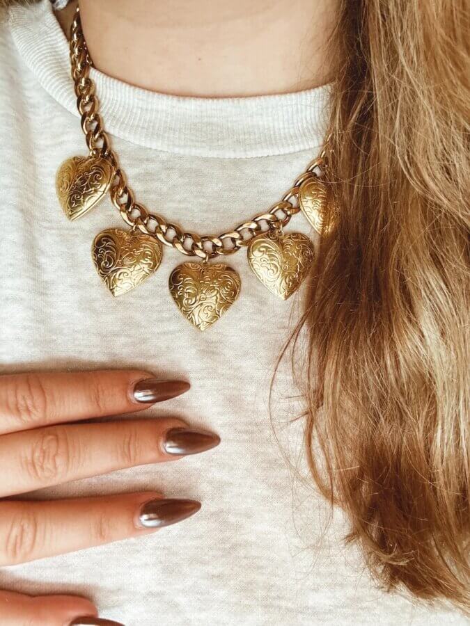 15 Memphis FINDS at Local Shops: Spring Dresses, Home Decor & More! - 9 A person wearing a gold chain necklace with five engraved heart pendants, a white top, and metallic brown nail polish showcases standout styleβone of the chic Memphis FINDS this April.