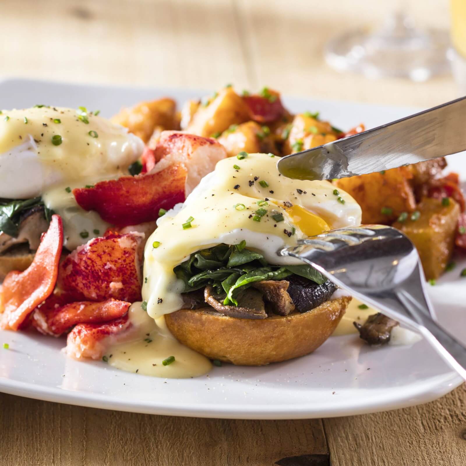 A close-up of eggs Benedict with lobster, sautéed spinach, and hollandaise sauce on an English muffin, served with roasted potatoes—an elegant Memphis-inspired dish perfect for Mother's Day Brunch.