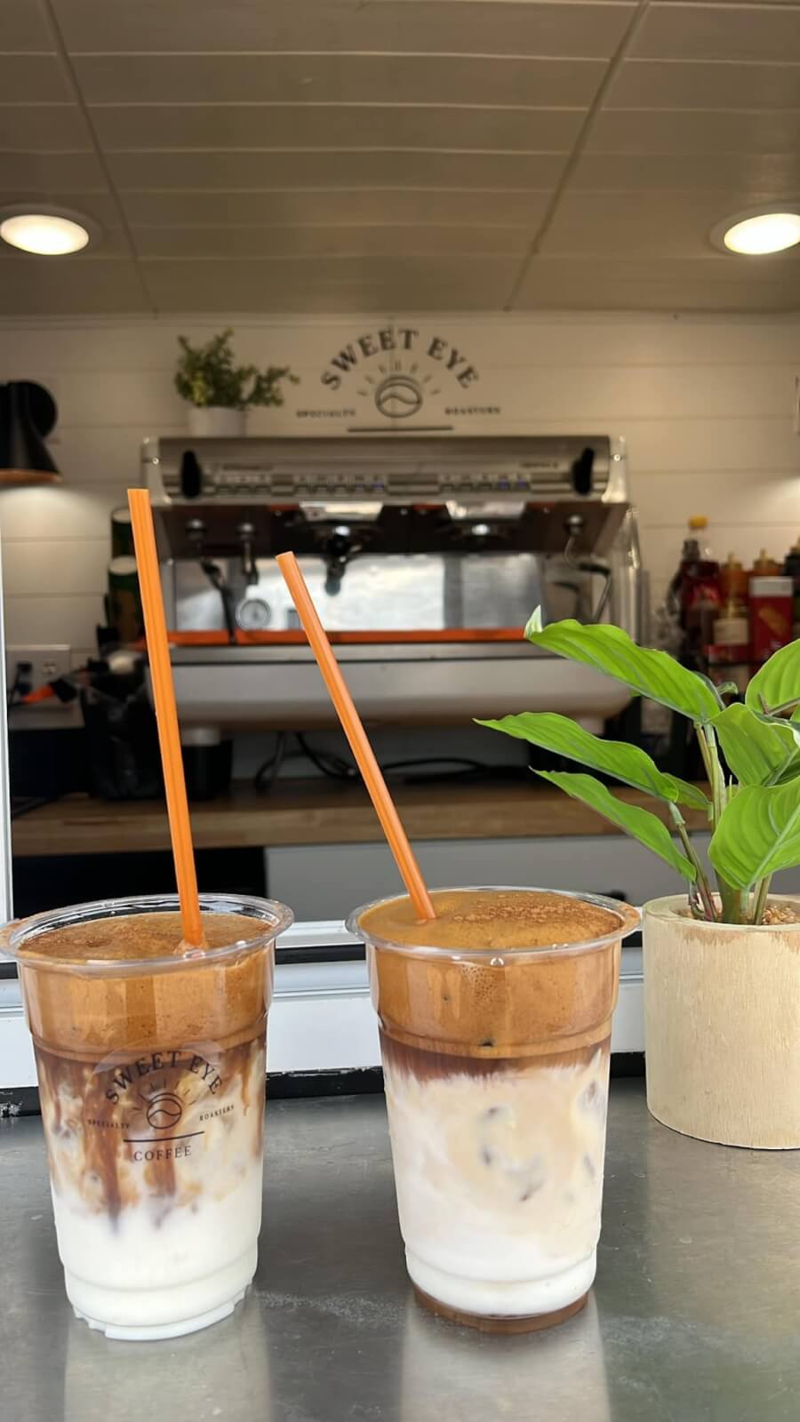 Two iced coffee drinks with orange straws sit on a counter in one of the new Memphis restaurants. A coffee machine and a potted plant provide a charming backdrop, capturing the essence of April's fresh beginnings.