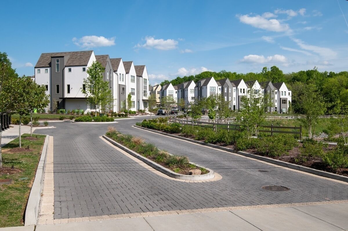 A residential neighborhood with modern, white, three-story townhouses, paved streets, and landscaped greenery—perfect for those seeking homes for sale in East Nashville under a clear blue sky.