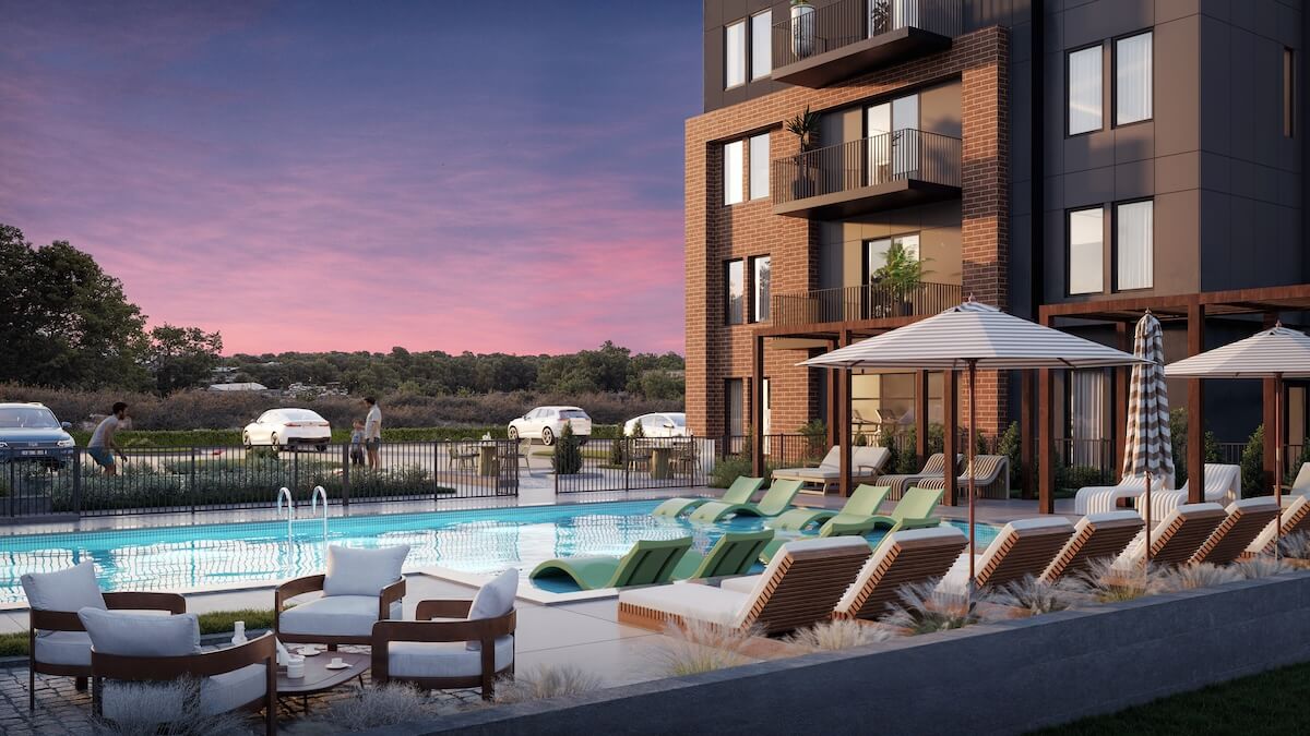 Modern apartment building with outdoor swimming pool, lounge chairs, umbrellas, and landscaped surroundings at dusk. Perfect for those seeking homes for sale in East Nashville, several people relax by the pool while cars are parked outside the fence.