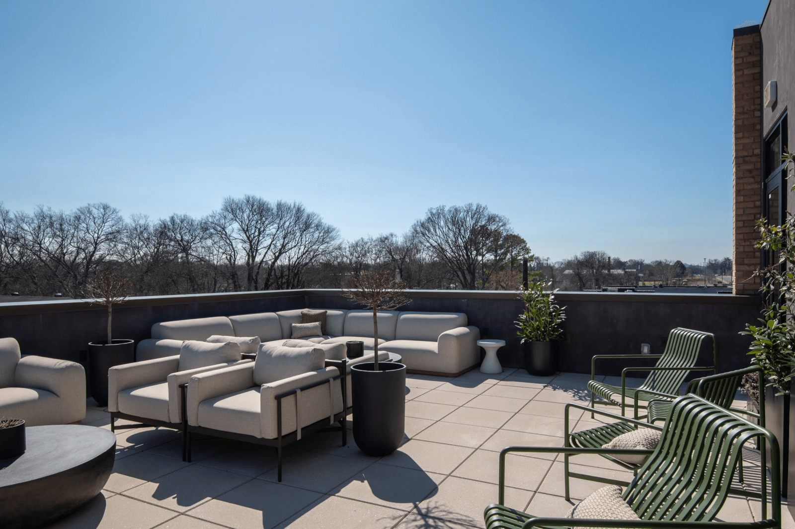 Modern outdoor rooftop patio in East Nashville with cushioned seating, metal lounge chairs, and potted plants—perfect for relaxing while overlooking the trees and clear blue sky. Ideal for those seeking homes in exciting new developments.