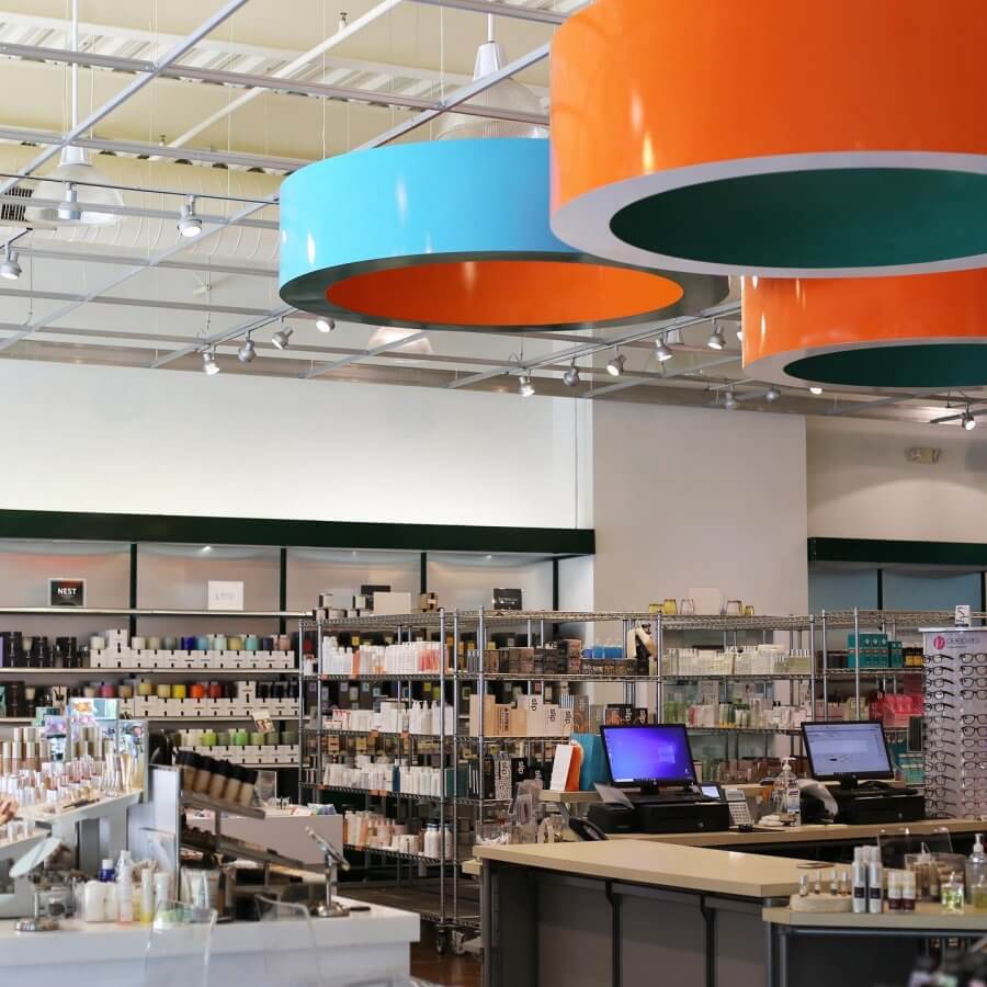 A well-lit store interior with shelves stocked with beauty and skincare products, two checkout counters, and large orange and blue circular ceiling fixtures—discover exclusive Nashville deals throughout the store.