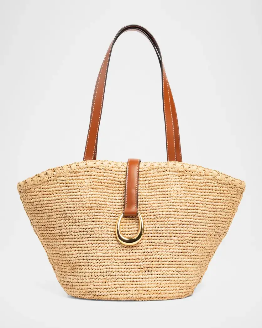 A woven straw tote bag with brown leather handles and a leather strap featuring a gold ring accent at the front—perfect for effortless summer style.
