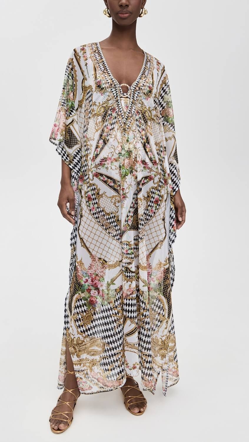 A stylish person wearing a long, loose-fitting kaftan with an ornate, multicolored pattern and gold accents, paired with strappy gold sandals—perfect for a vibrant summer look.