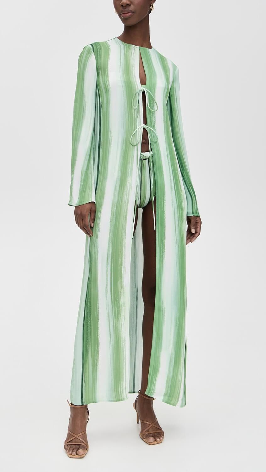 A stylish person wearing a long-sleeve, green and white striped maxi dress with front cutouts and ties, paired with strappy heeled sandals—perfect for a summer look.