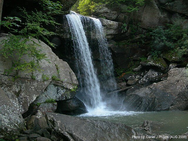 A waterfall cascades over a rocky ledge into a pool surrounded by large rocks and greenery, making it one of the best Kentucky hikes for nature lovers exploring scenic waterfall trails in Kentucky.