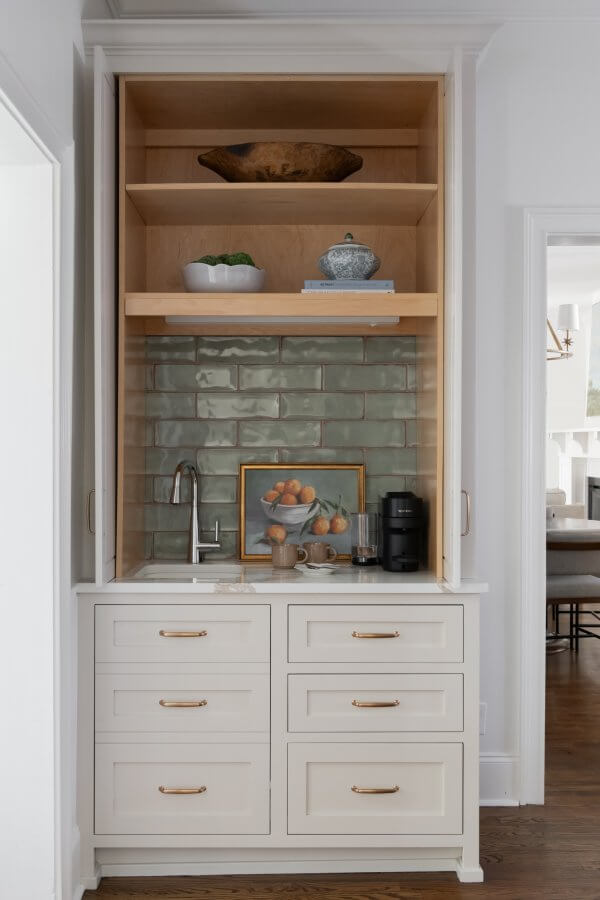This cozy Sylvan Park home features a charming kitchen nook with a green tile backsplash, white cabinets, and a small sink. The modern design is complemented by decorative shelves, a coffee maker, and touches like a framed painting.