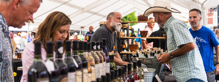 The Best Festivals in the South - 14 People browse and sell various bottled products under a white tent at an outdoor market, capturing the lively spirit found at the best festivals in the south.