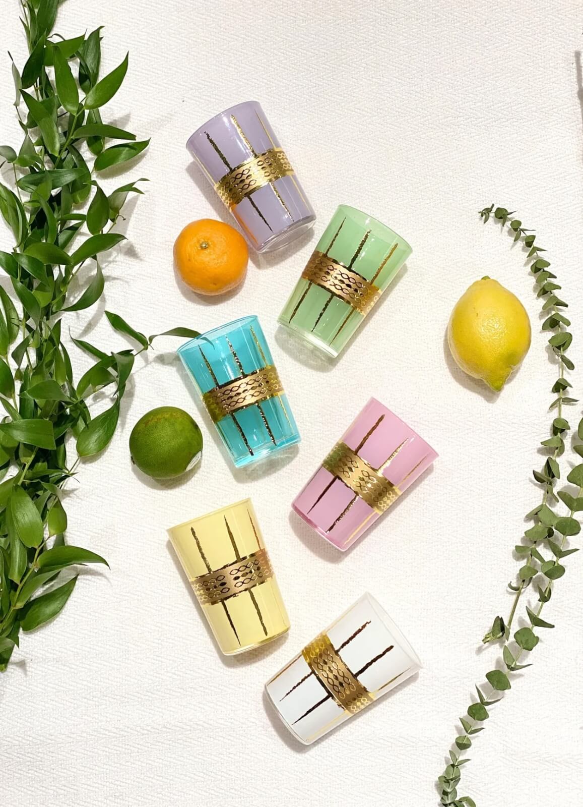 Six pastel-colored glasses with gold bands are arranged on a white surface with a lemon, lime, orange, and green leaves—perfect for Mother’s Day brunch or thoughtful grad gifts in Nashville.
