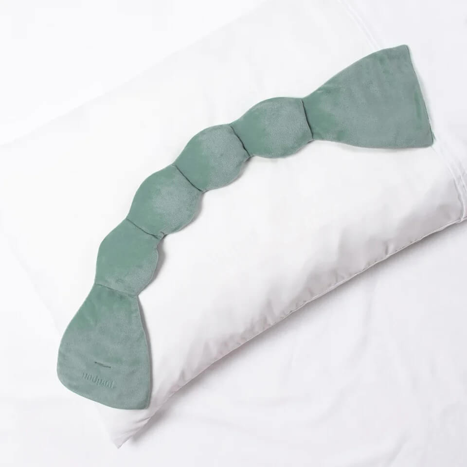 A segmented, green, bean-shaped pillow or cushion—perfect for Nashville-inspired decor or thoughtful Grad Gifts—rests atop a white standard pillow on a white bed.
