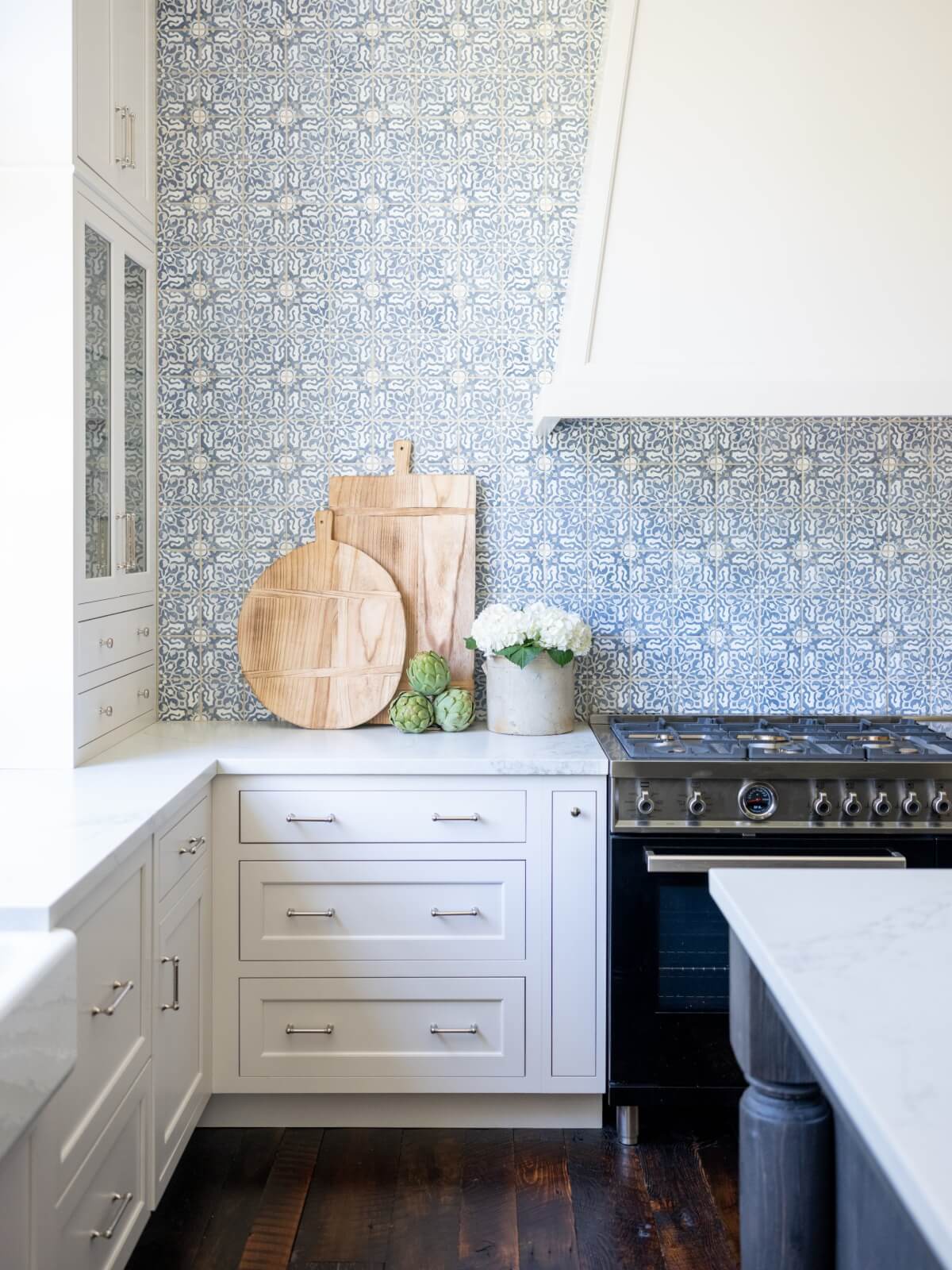 A kitchen with a blue-and-white patterned backsplash and white vent hood.