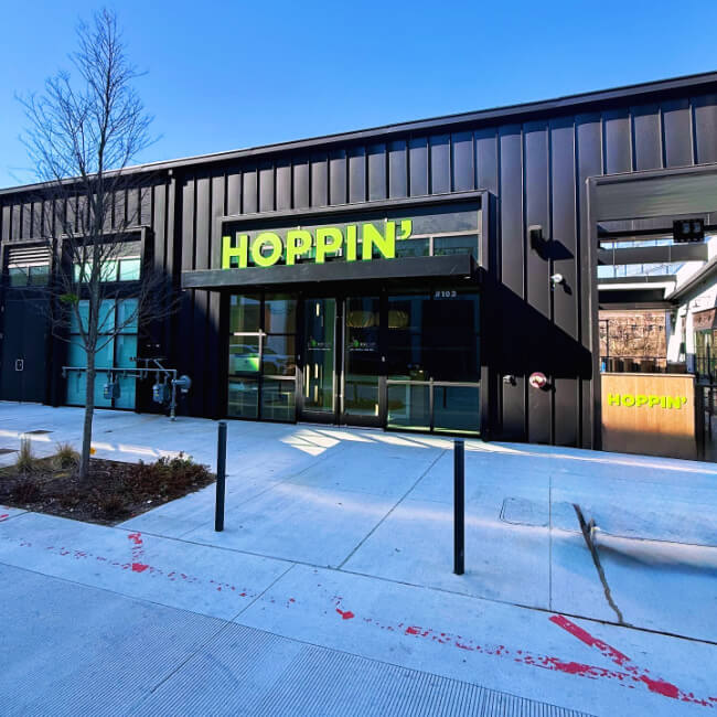 9 New Nashville Restaurants to Try This Month - 21 A modern black building with large windows and a bright green "HOPPIN’" sign above the entrance stands out among new Nashville restaurants on a sunny day.