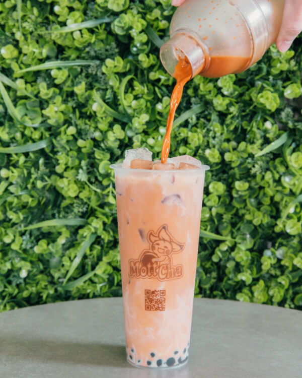 9 New Nashville Restaurants to Try This Month - 25 A hand pours Thai milk tea from a shaker into a clear cup with ice and tapioca pearls, set on a table in front of a green leafy background.