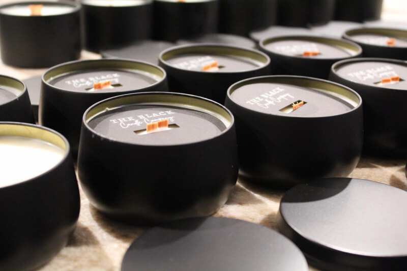 Several black candles with wooden wicks and lids are arranged on a surface.